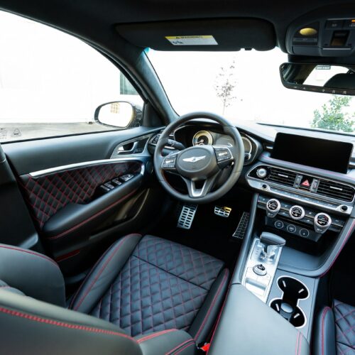 Genesis G70 3.3t photographed from the rear seat showing the interior, front seat, console, and steering wheel.