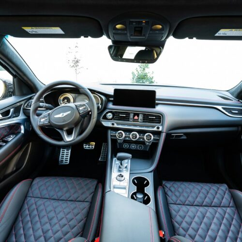 Genesis G70 3.3t photographed from the rear seat showing the interior, front seat, console, and steering wheel.