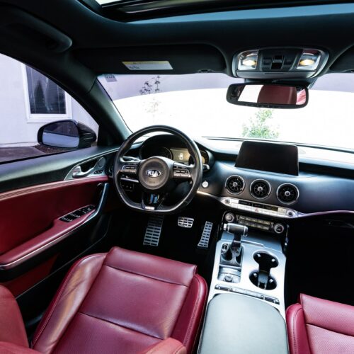 Kia Stinger photographed from the rear seat showing the interior, front seat, console, and steering wheel.