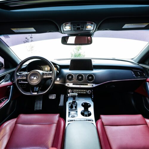 Kia Stinger photographed from the rear seat showing the interior, front seat, console, and steering wheel.