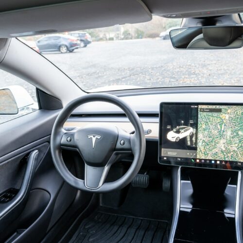 Tesla Model 3 photographed from the rear seat showing the interior, front seat, console, and steering wheel.