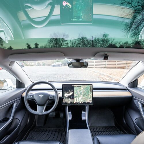 Tesla Model 3 photographed from the rear seat showing the interior, front seat, console, and steering wheel.