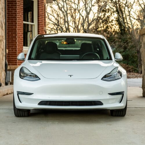 Tesla Model 3 parked on a forested driveway photographed from the front.